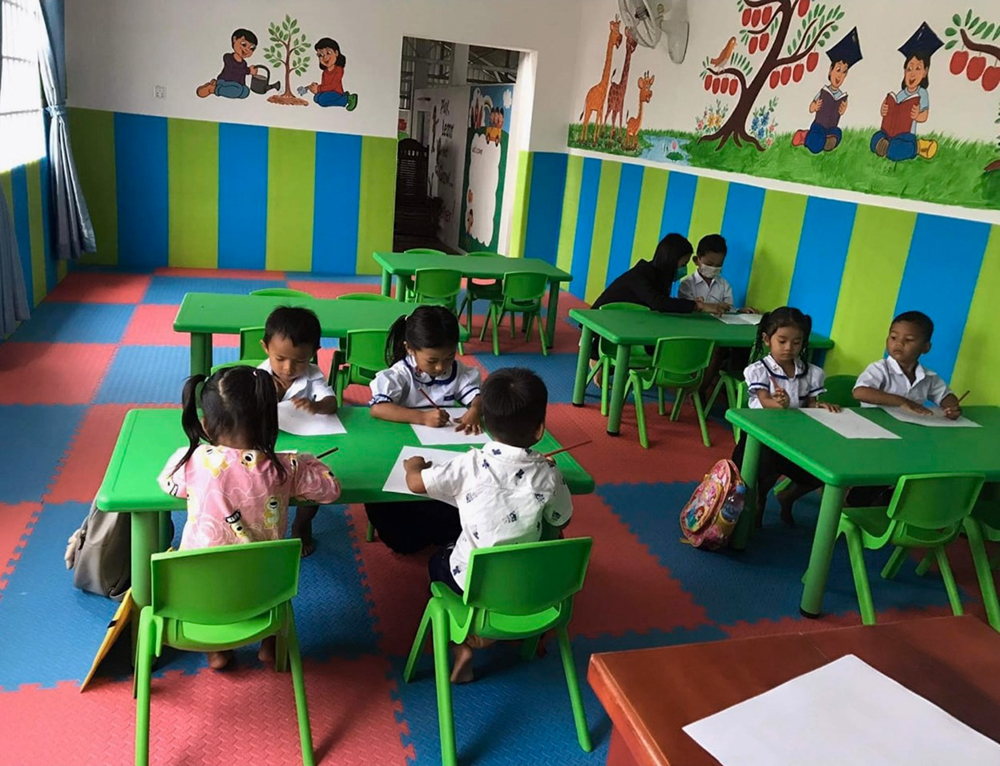 Sieben Kinder mit einer Betreuerin beim Malen und Üben. In diesem Raum findet auch die Vorschule der älteren Kinder statt.